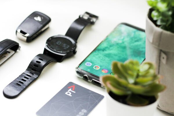 black Android smartphone near round black smartwatch, car fob, leather watch, and green succulent plant
